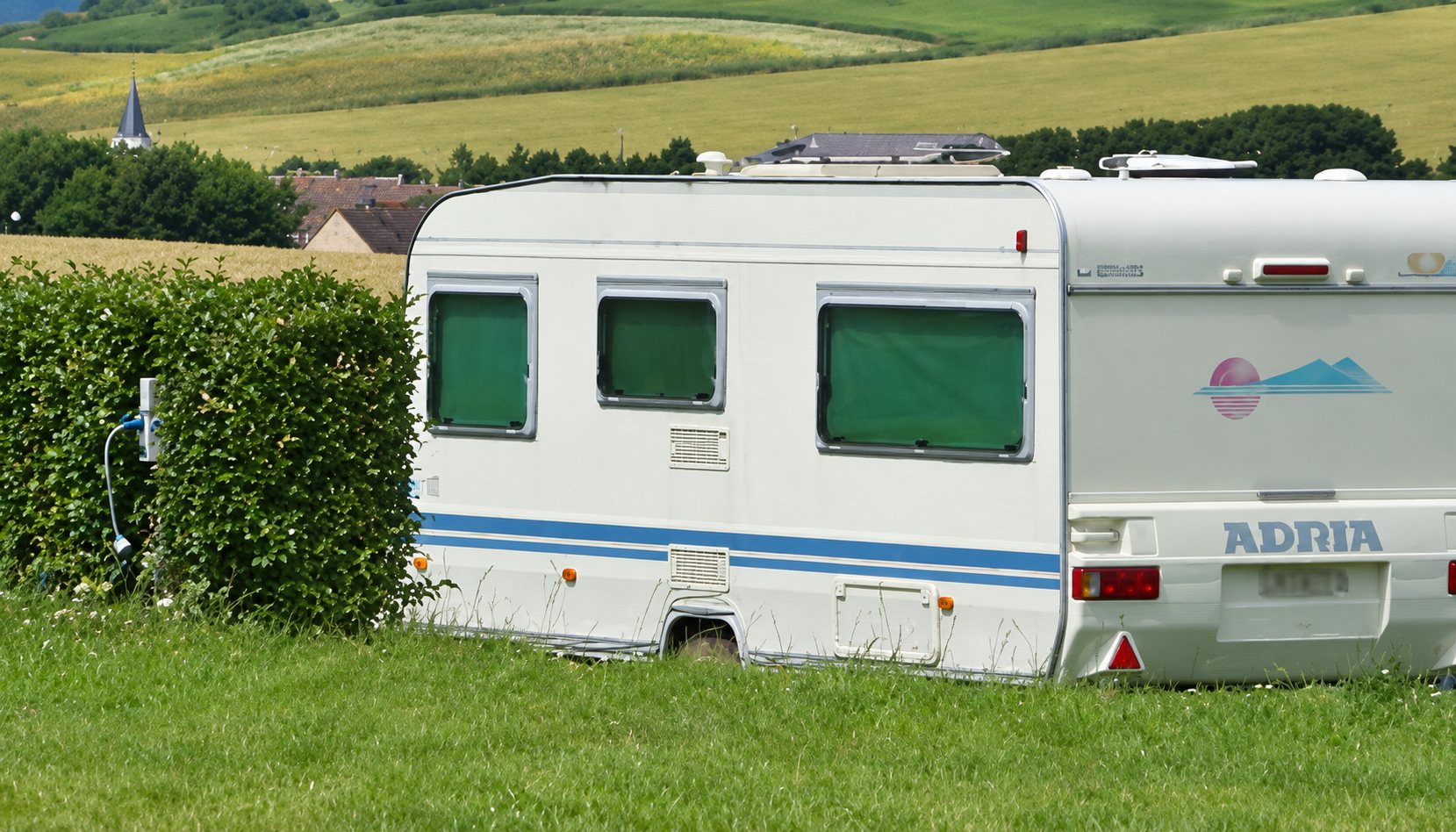 Caravane blanche garée sur un terrain herbeux devant une haie