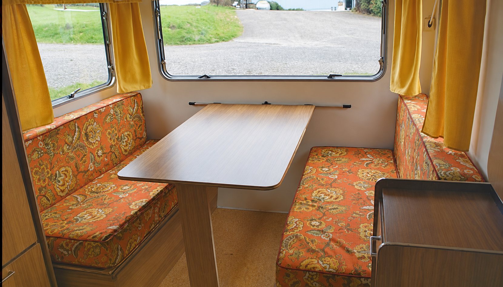 Intérieur de la caravane 3, banquettes fleuries et table en bois