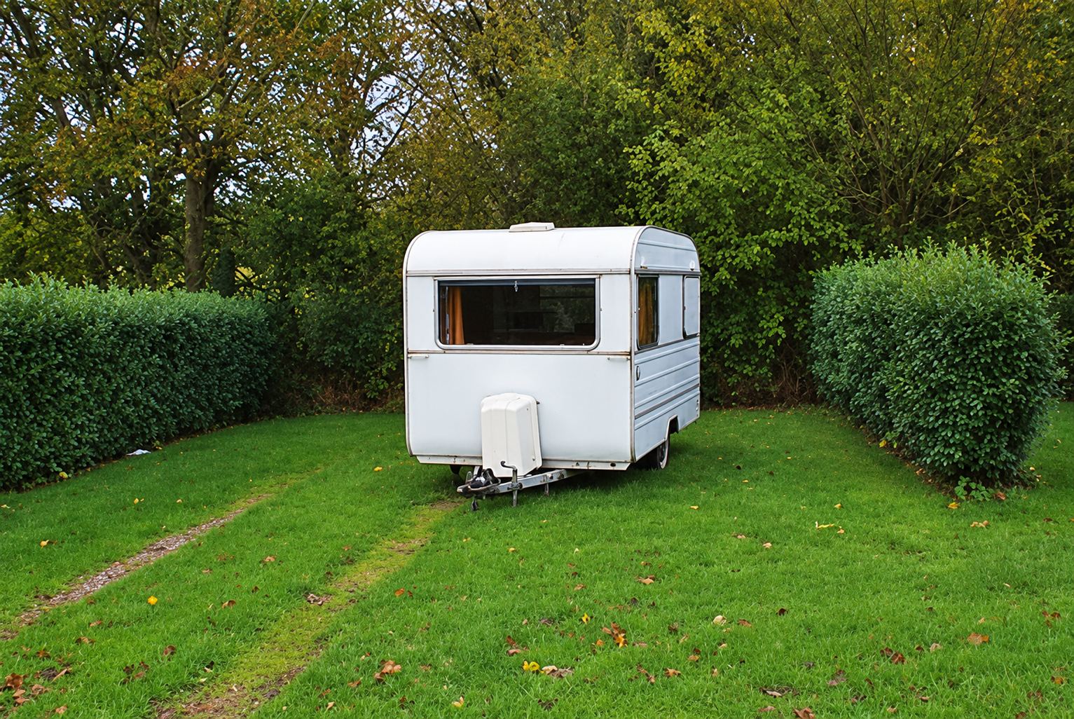 Petite caravane blanche vintage sur une pelouse entourée de haies